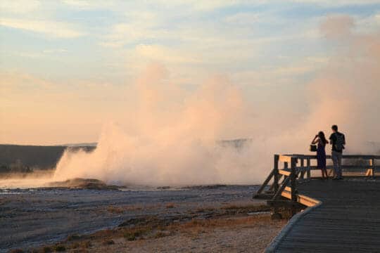 A Couple Stands At The Edge Of The Boardwalk To Watch Geysers Erupting At The Lower Geyser Basin In Yellowstone National Park