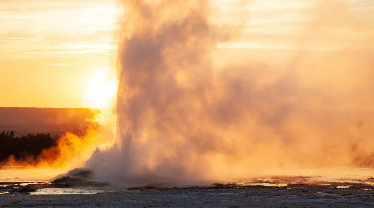 A Geyser Erupts In An Orange Glow As The Sun Sets On The Lower Geyser Basin In Yellowstone National Park