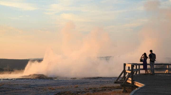 A Couple Stands At The Edge Of The Boardwalk To Watch Geysers Erupting At The Lower Geyser Basin In Yellowstone National Park