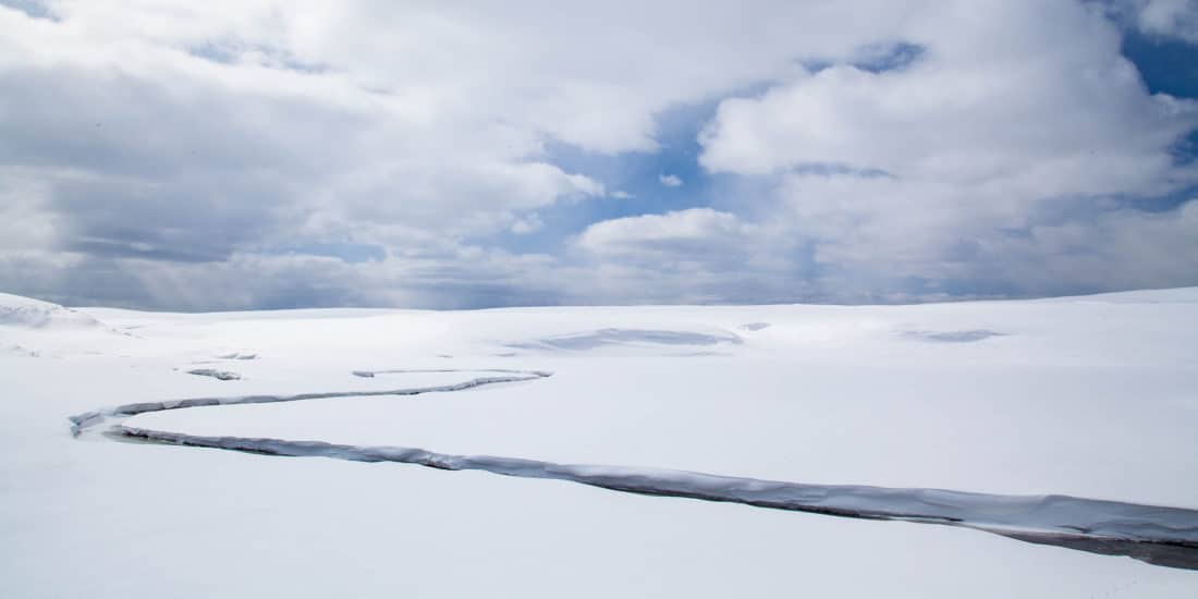 A Creek Runs Freely In The Middle Of A Snowy White Landscape Outside Of Big Sky Montana