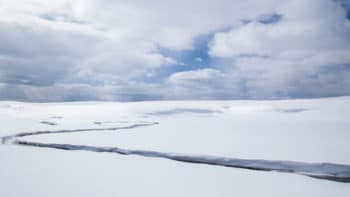 A Creek Runs Freely In The Middle Of A Snowy White Landscape Outside Of Big Sky Montana